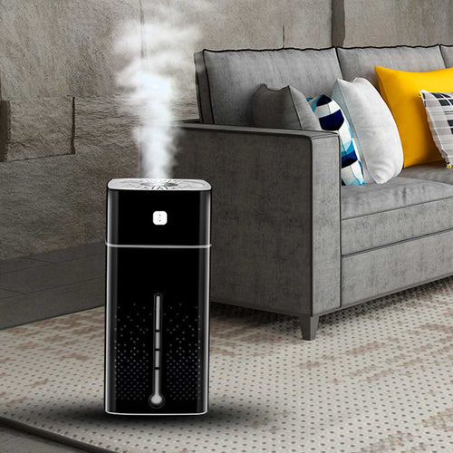Black humidifier emitting steam in a living room with a gray sofa and colorful pillows.