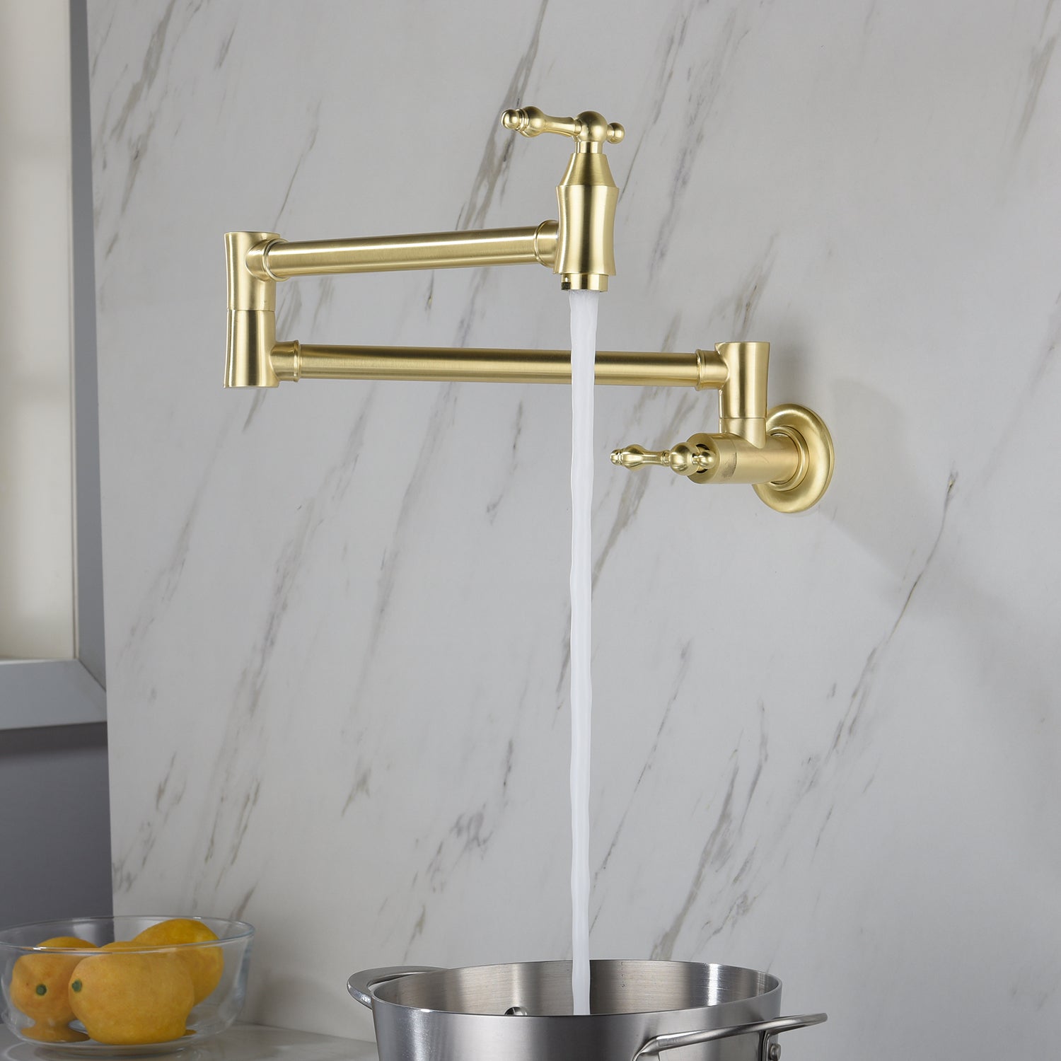 Gold wall-mounted kitchen faucet with water flowing into a pot against a marble wall.